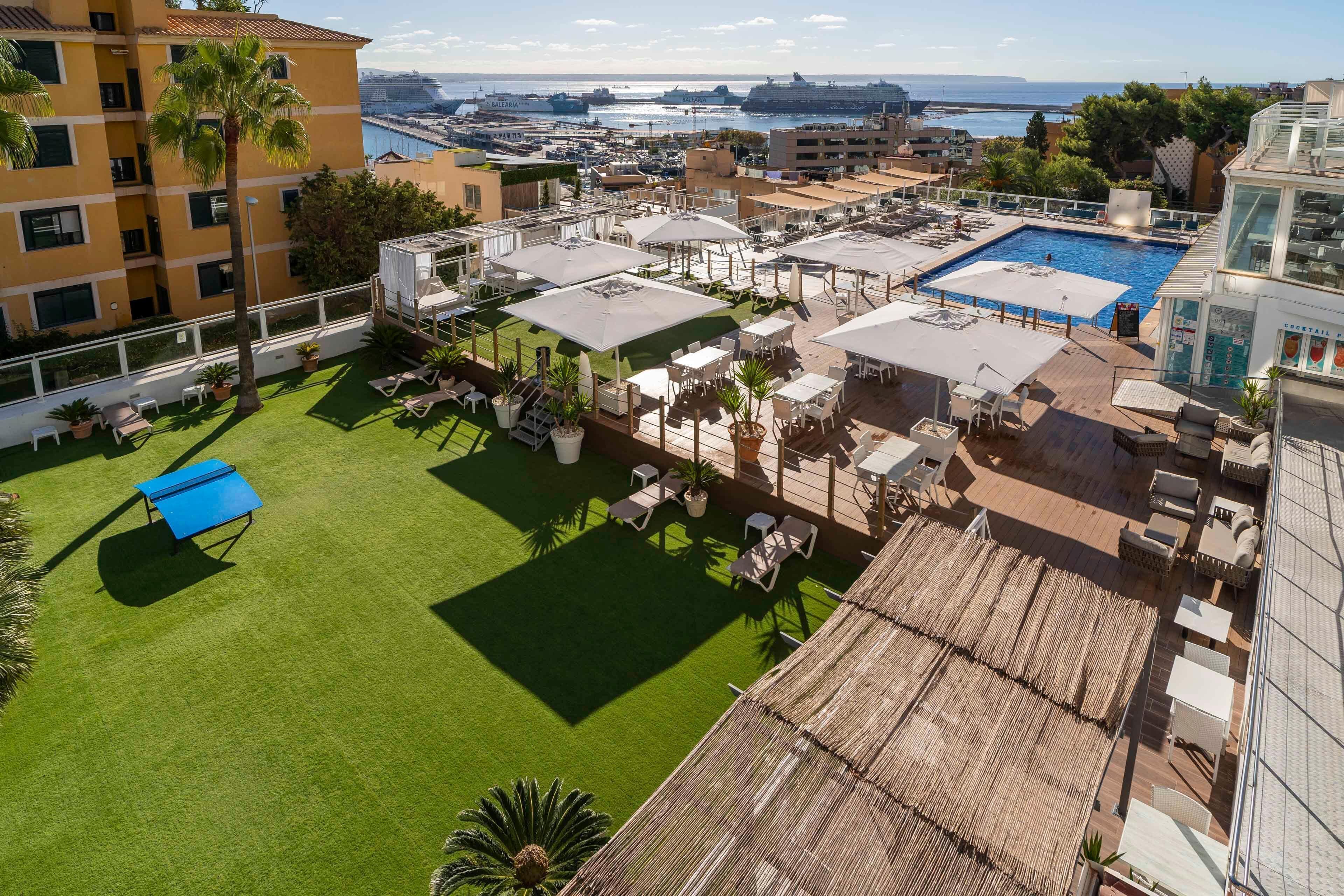 Zona de piscina en la azotea con sillones de descanso y sombrillas, rodeada de edificios y vista al mar.