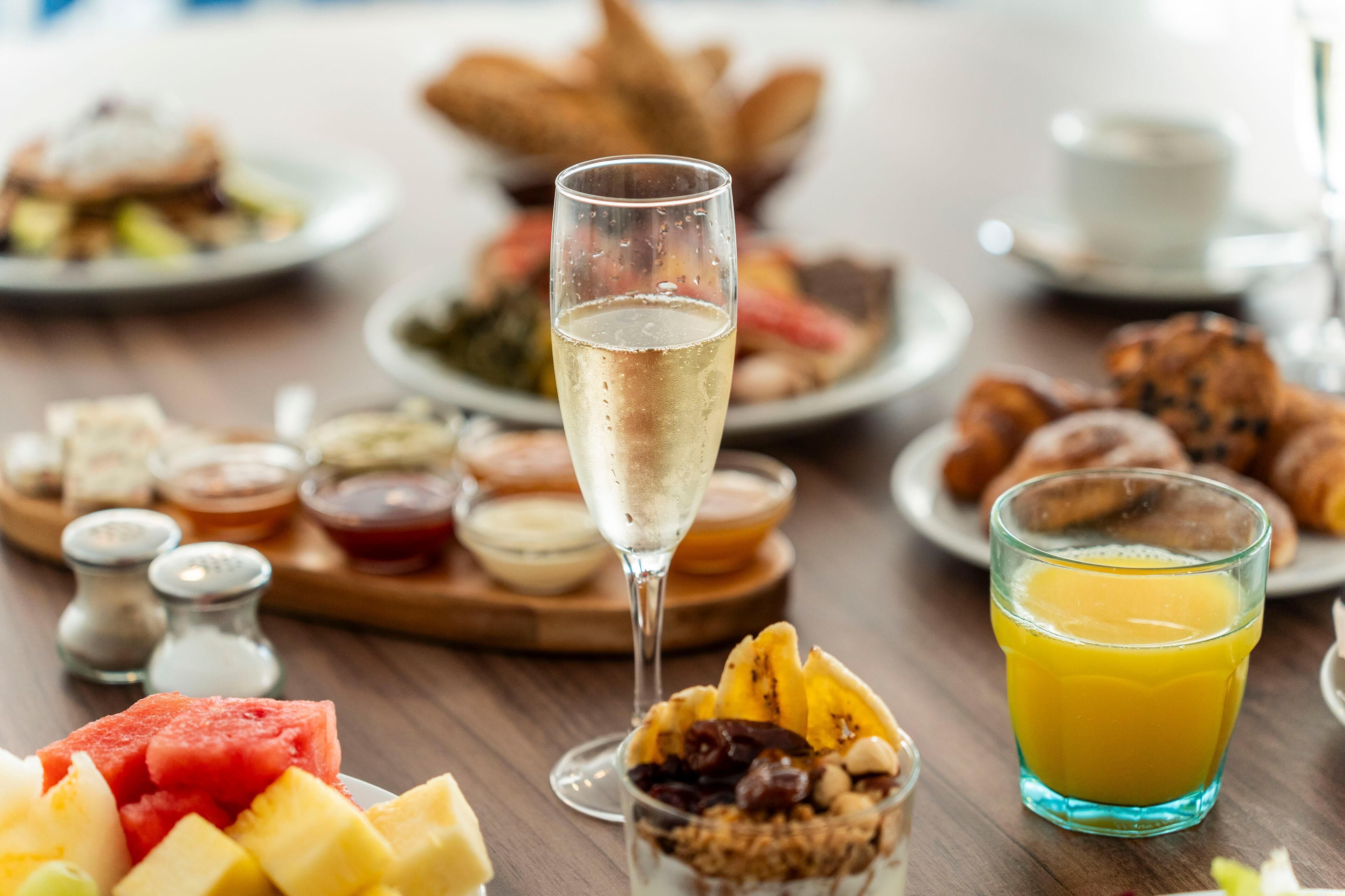 Una mesa de desayuno con diversos platos, un vaso de zumo de naranja y una copa de champán.