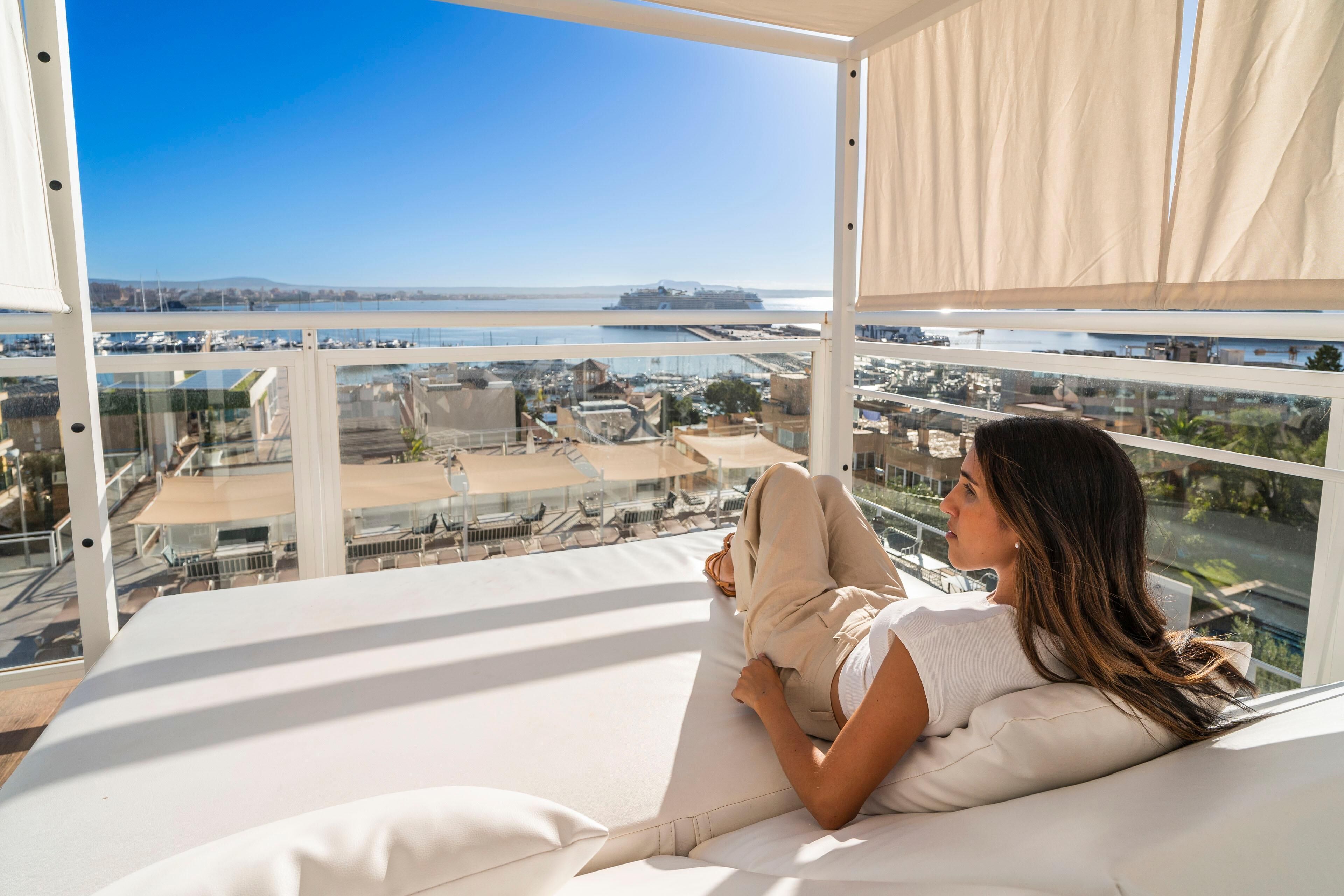 Una persona descansando en una cama con vistas a un puerto deportivo y al paisaje urbano.