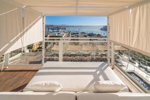 Un balcón con vista a un puerto deportivo y barcos, una terraza de madera y un sofá blanco con cojines.