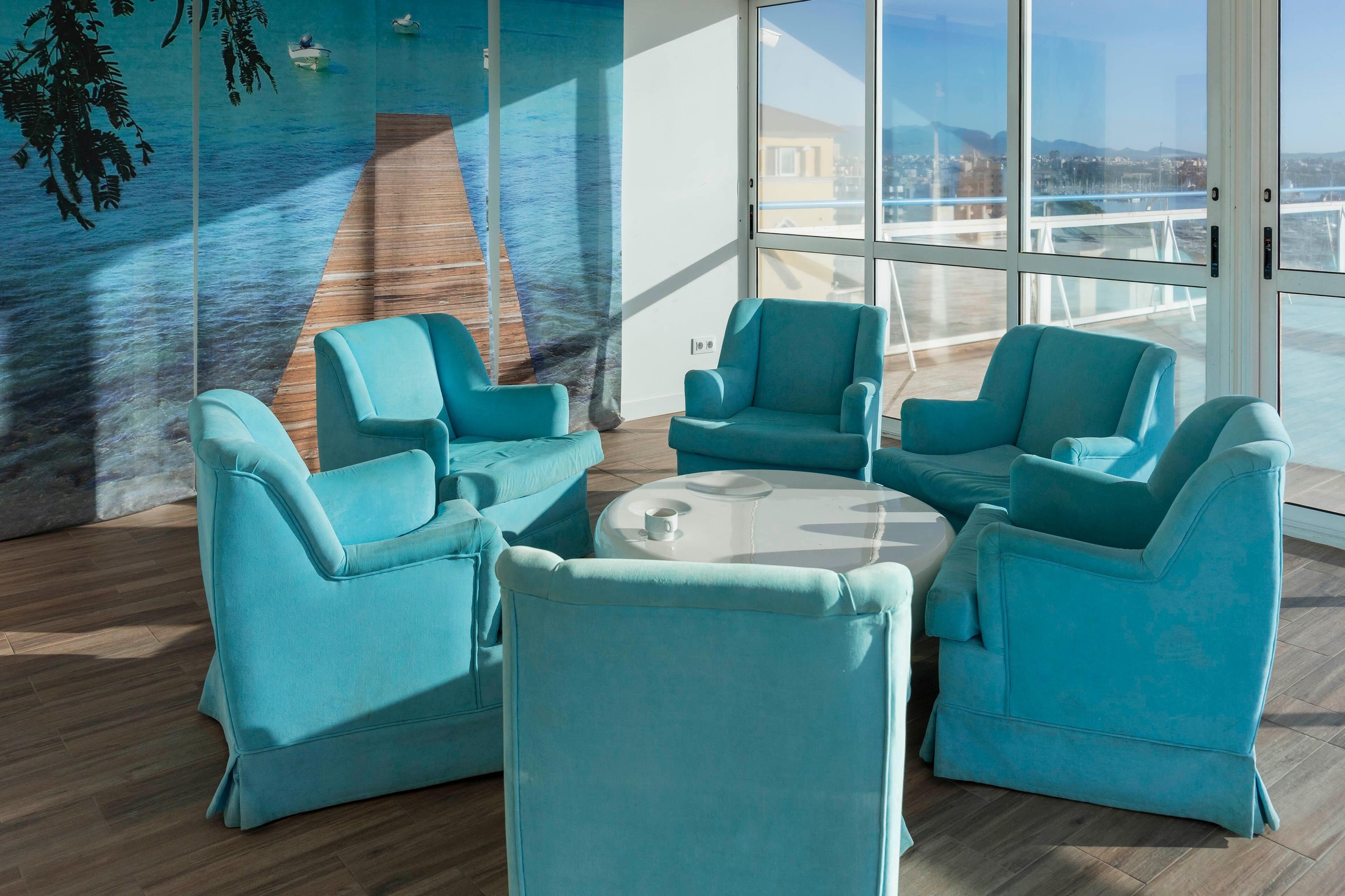 Eine moderne Lounge mit Türkis-Sesseln und einem runden Tisch, große Fenster mit Blick auf eine Brücke und eine Skyline.