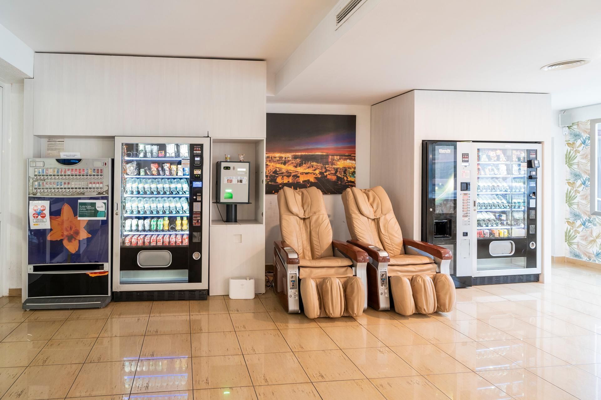 A clean lobby with two massage chairs, a vending machine, and a wall-mounted massage device.