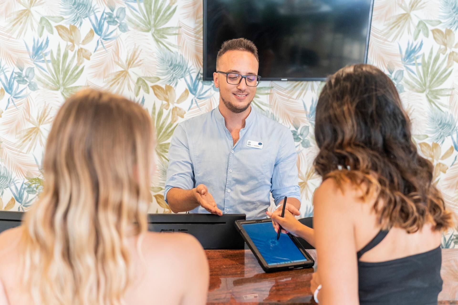 Un espace d’accueil d’hôtel avec un membre du personnel assis derrière un comptoir, un ordinateur portable et une étiquette nominative.