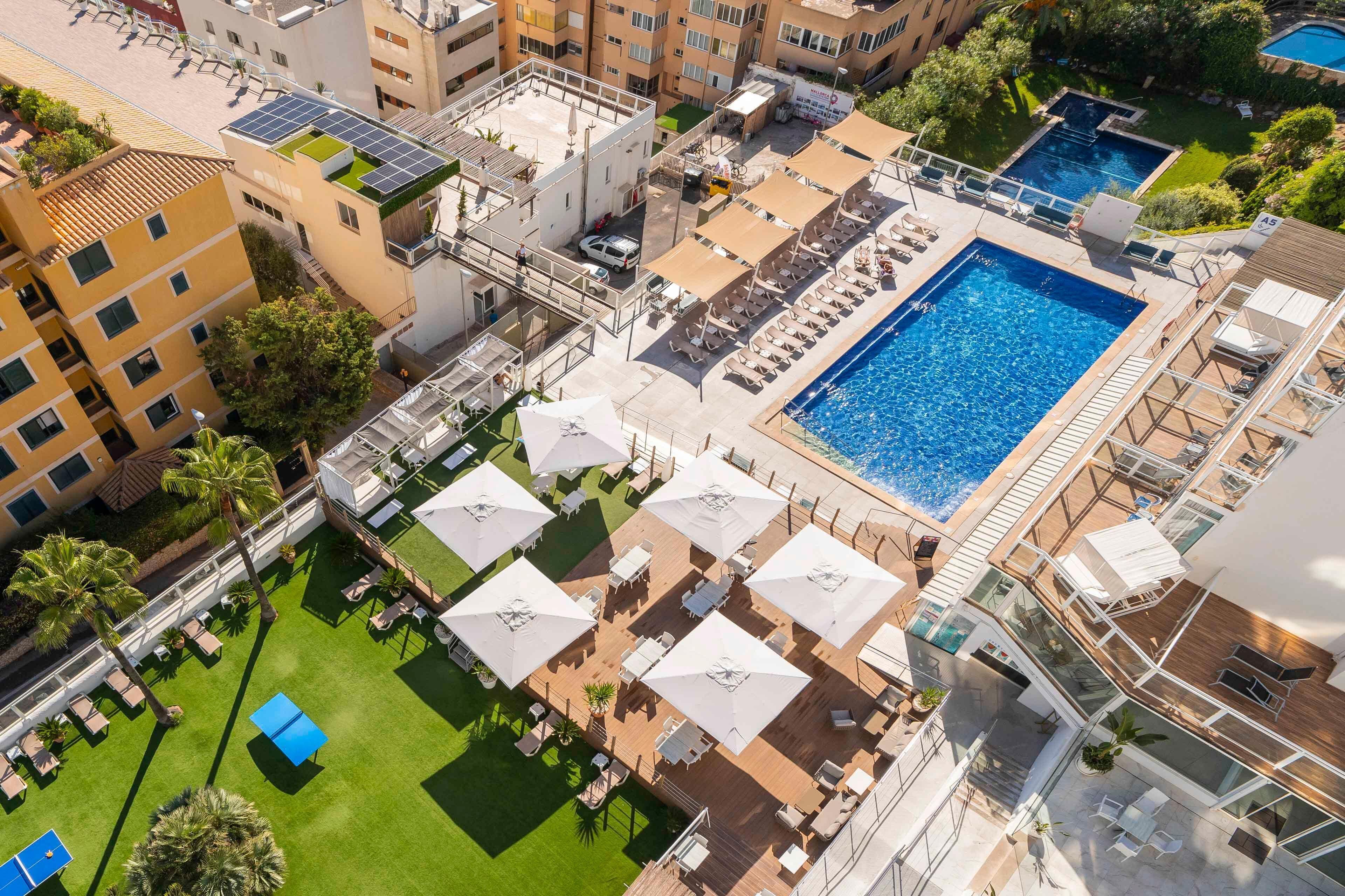 Un espace piscine aménagé sur le toit, doté de plusieurs chaises longues et de parasols, et entouré d’immeubles.