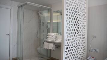 Un baño moderno con ducha envuelta en vidrio, un separador decorativo blanco y un pequeño tocador con toallero.