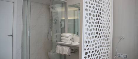 Een moderne badkamer met een douchecabine van glas, een witte decoratieve scheiding en een klein wastafelmeubel met een handdoekhouder.