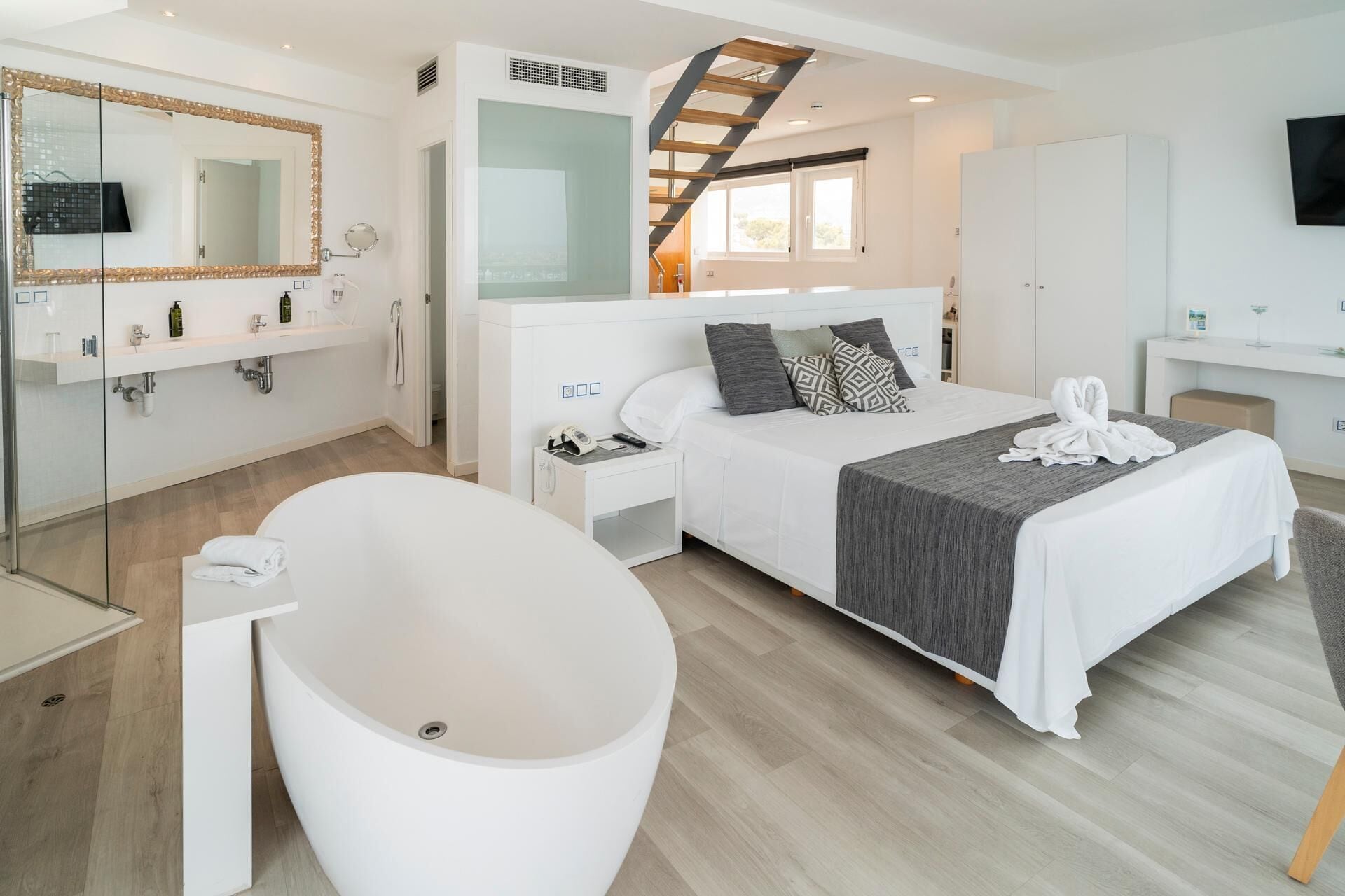 Een moderne hotelkamer met een groot bed, een aparte badkamer met een badkuip, een inloopkast en een trap naar een hoger niveau.