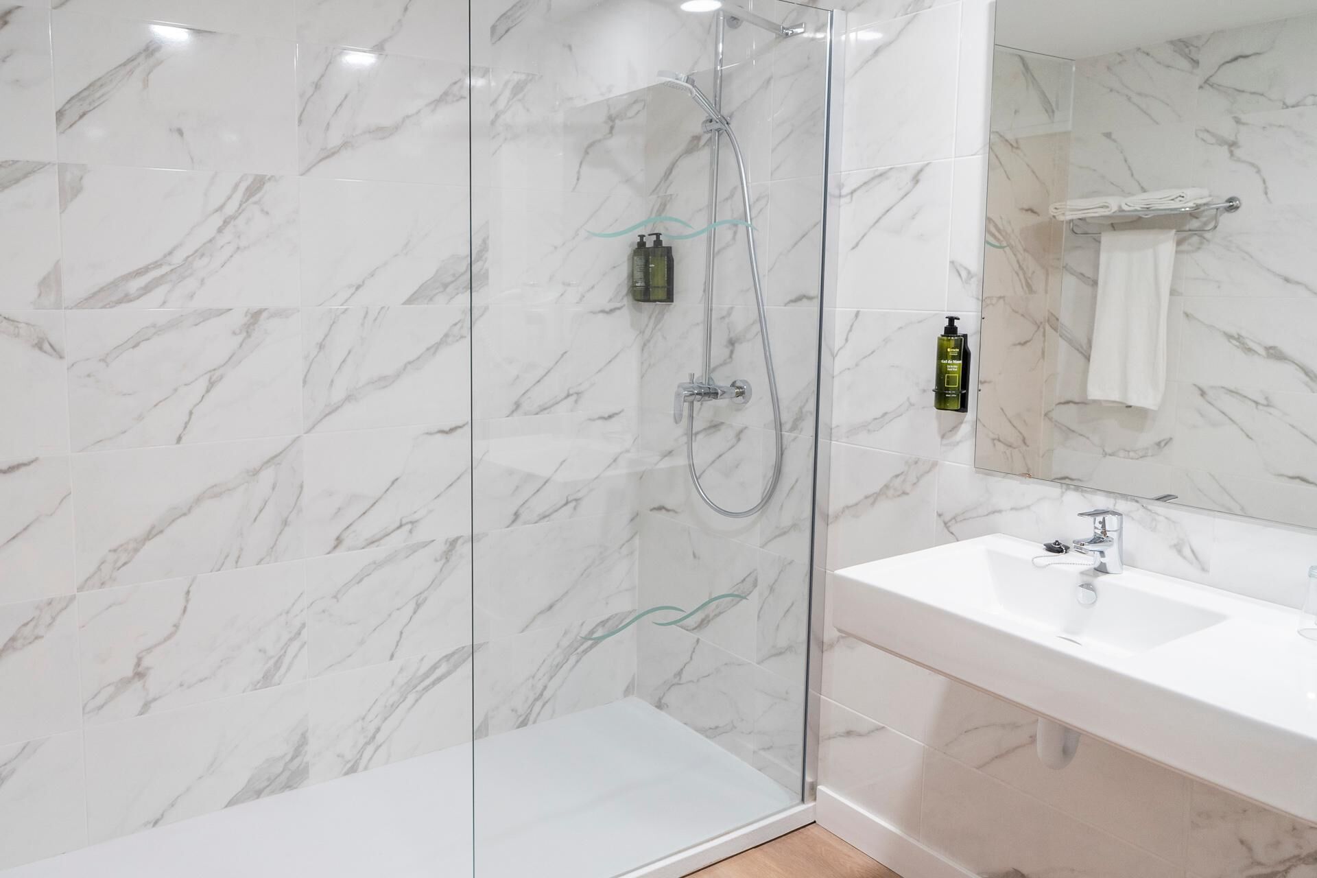 Un baño moderno con ducha envuelta en vidrio, lavamanos blanco y paredes con diseño de mármol.