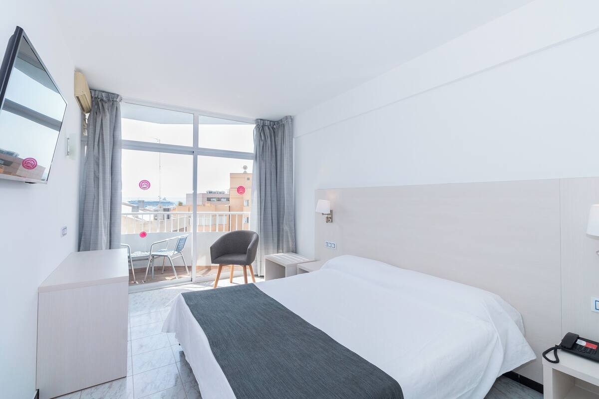 Une chambre d’hôtel avec un grand lit, un bureau, une chaise, une télévision et un balcon offrant une vue sur la ville.