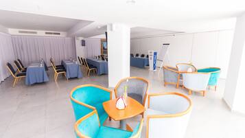 Un moderno vestíbulo de hotel con un área de descanso que incluye sillas azul verdoso y blancas, una pequeña mesa con un florero y un mostrador de recepción con mantel azul.
