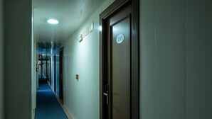 A hotel hallway with a blue carpet, a wooden door with a number plate, and a light fixture on the ceiling. - Hotel Bedoya (Santander)