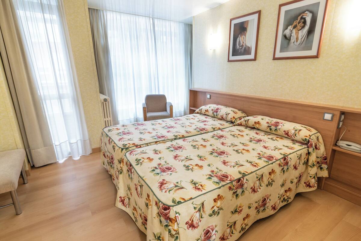 A hotel room with a double bed, a chair, a bedside table, and a wall-mounted telephone.