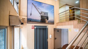 A modern elevator with a digital display, a staircase with metal railings, and a large window with a view of a crane and water. - Hotel Bedoya (Santander)
