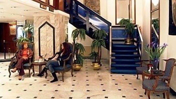 Un vestíbulo con piso de mármol, una escalera y zonas de estar con plantas.