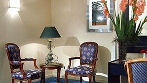 Habitación de hotel con dos sillones tapizados, una mesita con lámpara y un florero con flores.