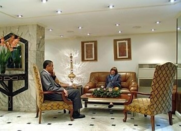 A formal meeting room with two chairs, a table with a floral arrangement, and a decorative lamp.