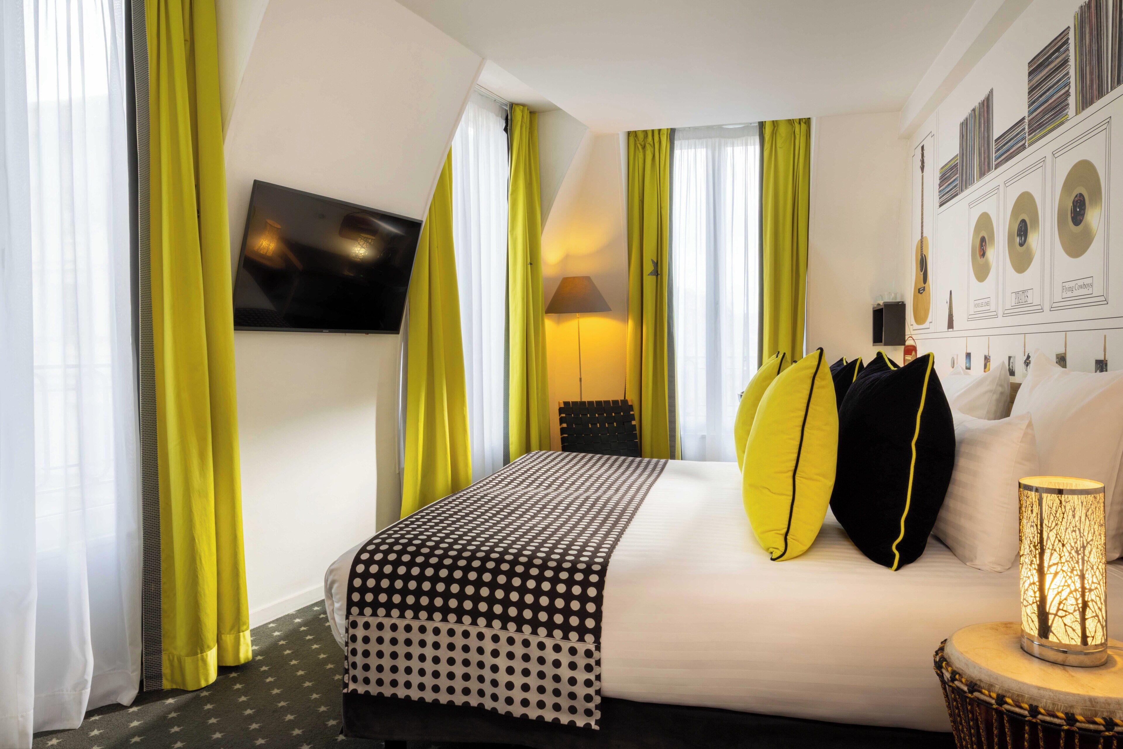 A hotel room with a bed, a lamp, a wall-mounted TV, and curtains.