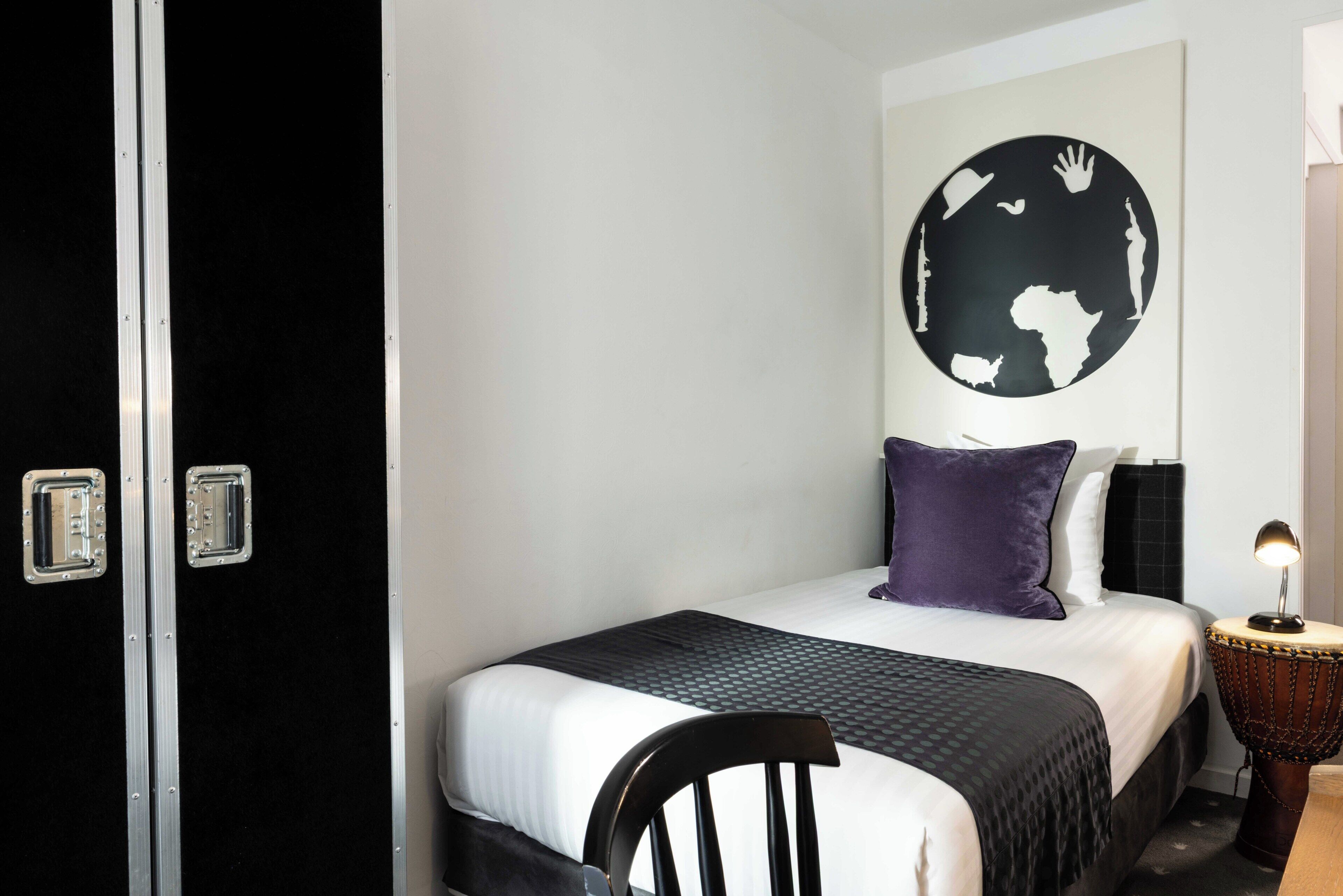 Une chambre d’hôtel avec un lit, un globe terrestre fixé au mur, une chaise, une petite table avec une lampe et une porte.