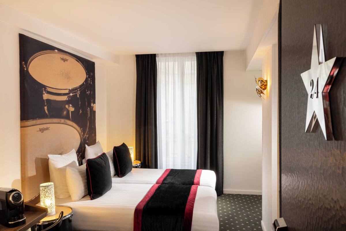 A hotel room with a bed, a drum set poster, a star-shaped decoration, and a lamp on the side table.