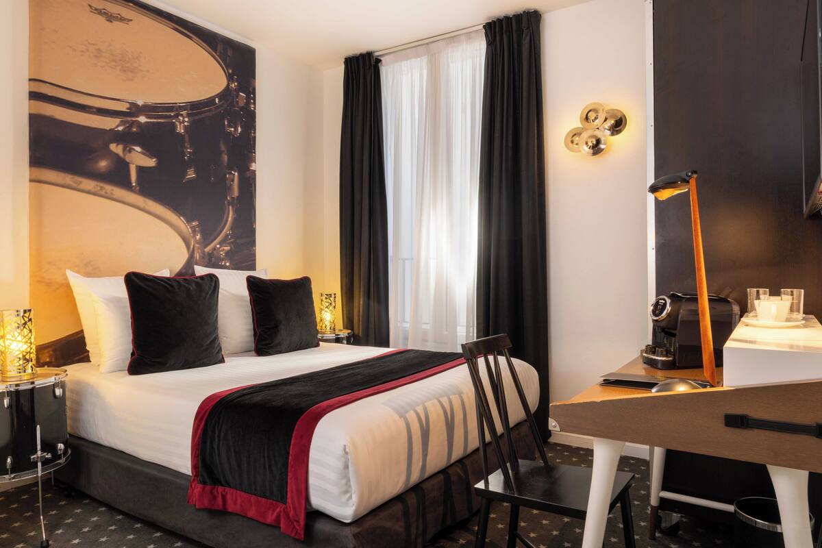 A hotel room with a bed, a desk, a chair, a lamp, and a wall-mounted light fixture.