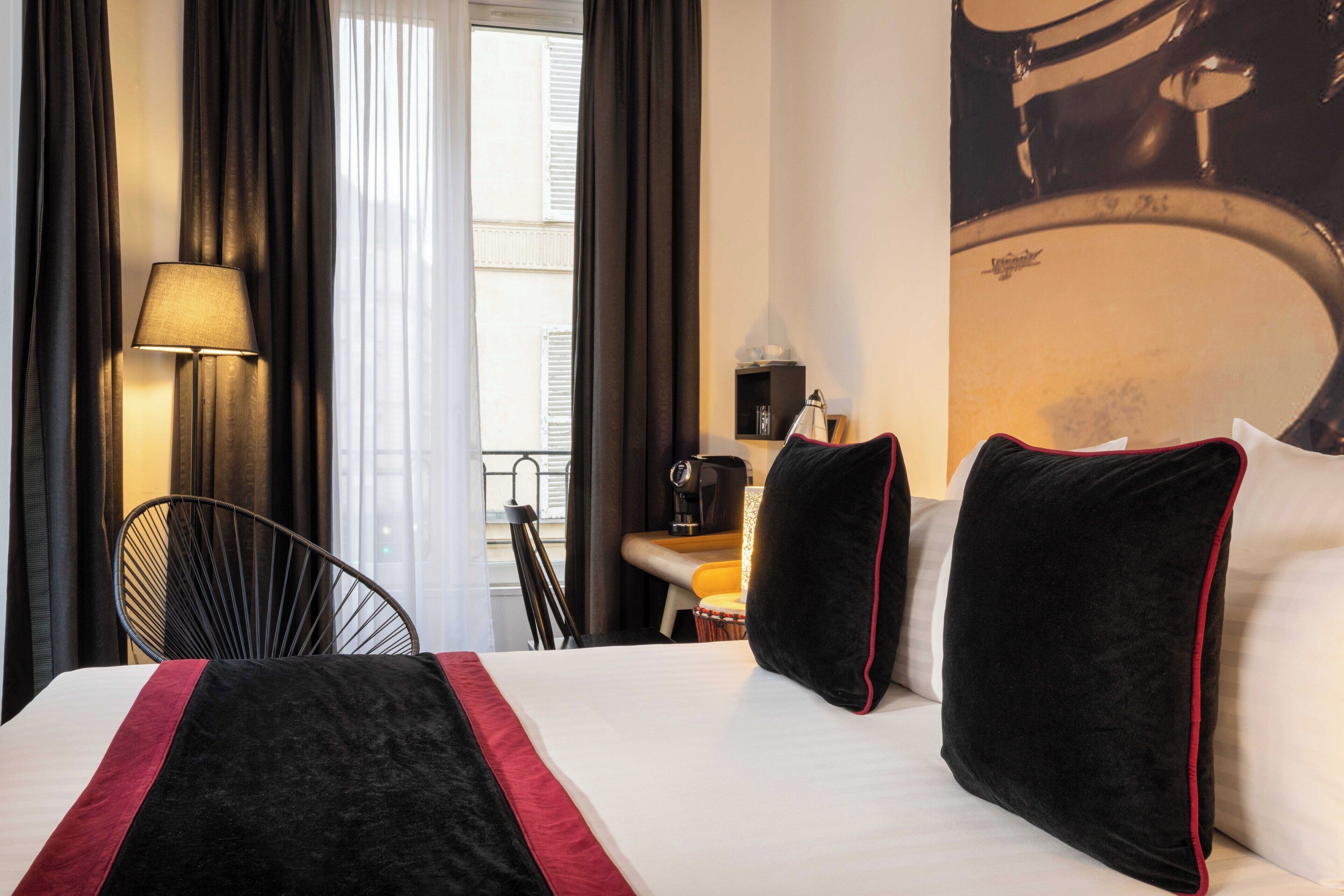A hotel room with a bed, a desk, a lamp, and a view of the city.