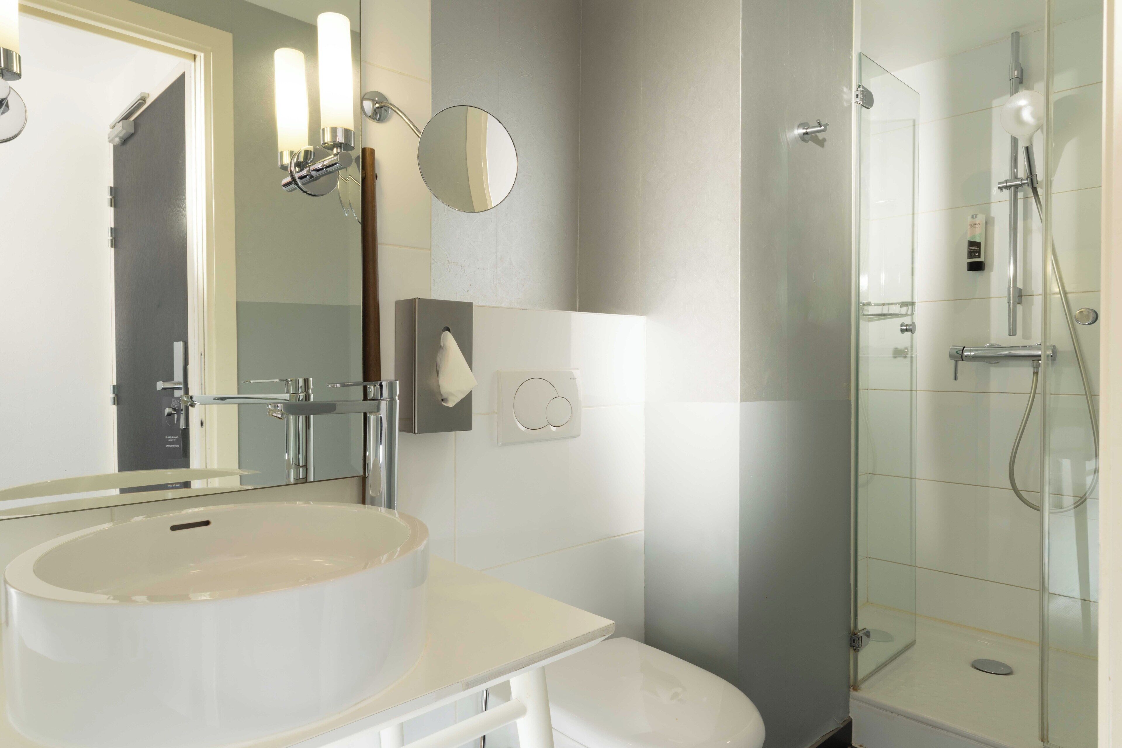A bathroom with a sink, toilet, mirror, and glass-enclosed shower.