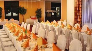 A banquet hall with long tables set for a formal event, featuring white tablecloths and orange napkins.