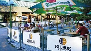 An outdoor seating area with tables and chairs, a Pilsner Arquette sign, and Globus Hotel signage. - Hotel Globus (Prague)