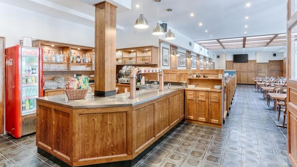 A spacious cafe with wooden furniture, a central counter, and a Coca-Cola refrigerator. - Hotel Globus (Prague)