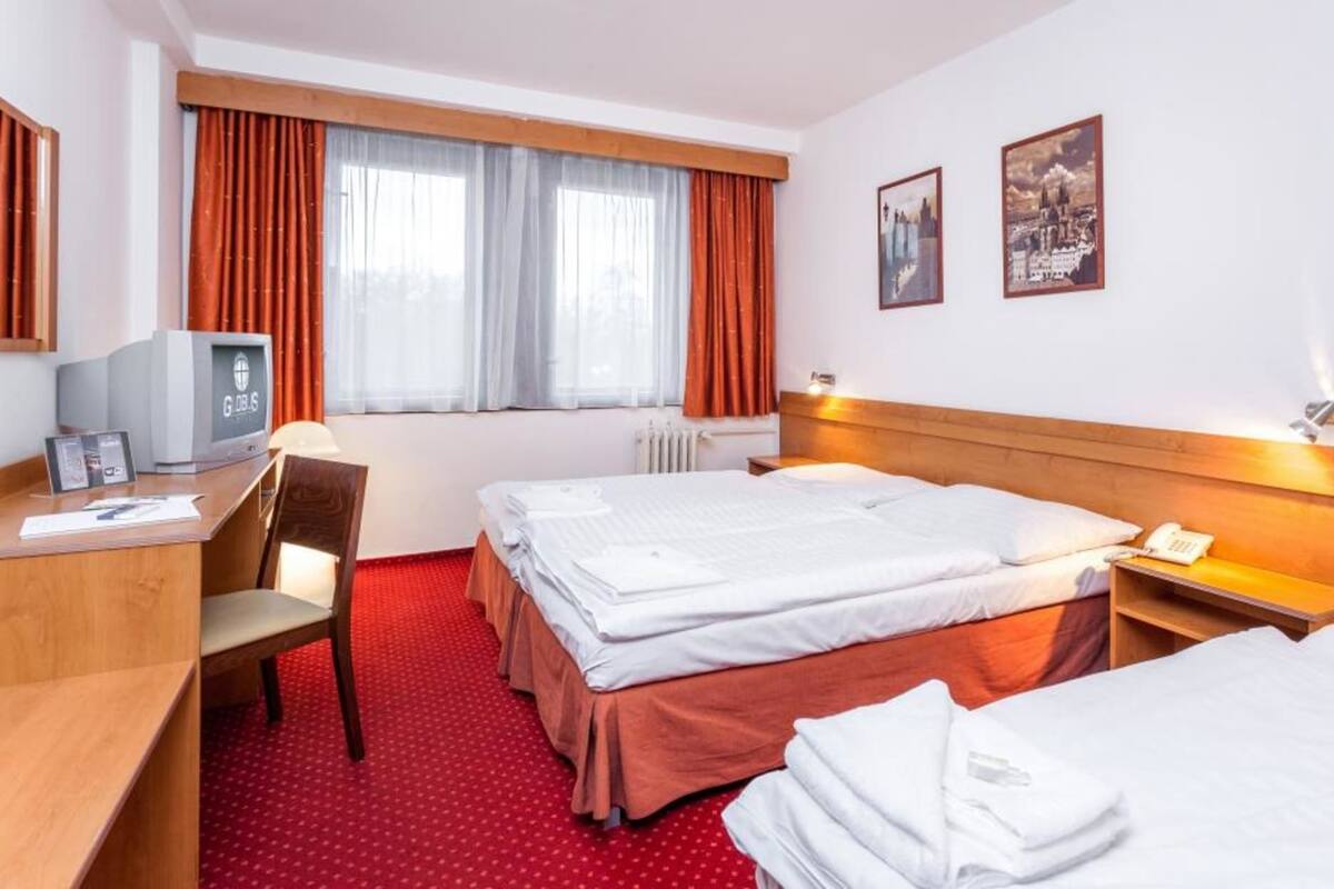 A hotel room with two beds, a desk, a chair, a television, and two framed pictures on the wall.
