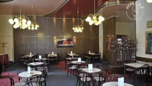 Un restaurant amb taules i caires rodones, llüsteres penjants i un quadre gran a la pared.
