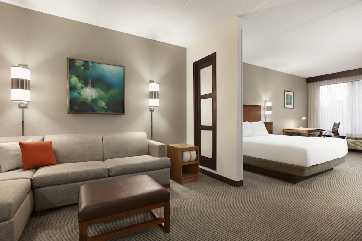 Quarto de hotel com sofá, cama, mesa de cabeceira e um quadro na parede.