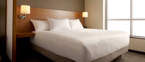 A hotel room with a bed, two bedside lamps, a wooden headboard, and a large window.