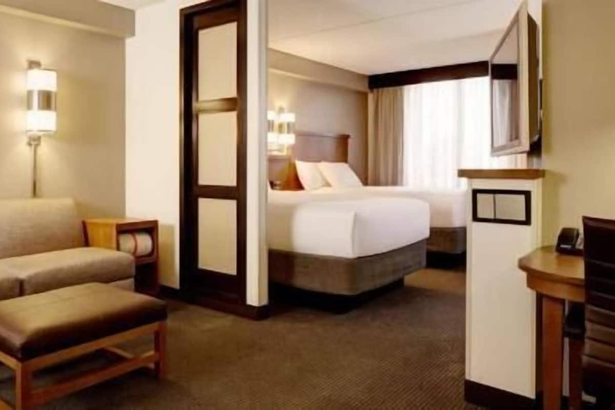 Quarto de hotel com cama, sofá, poltrona, escrivaninha e um quadro na parede.