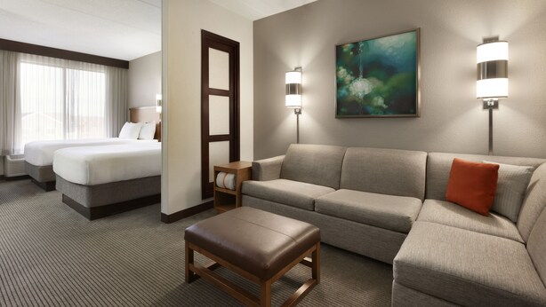 Une chambre d’hôtel comprenant un lit, un canapé, un pouf et deux lampes fixées au mur.