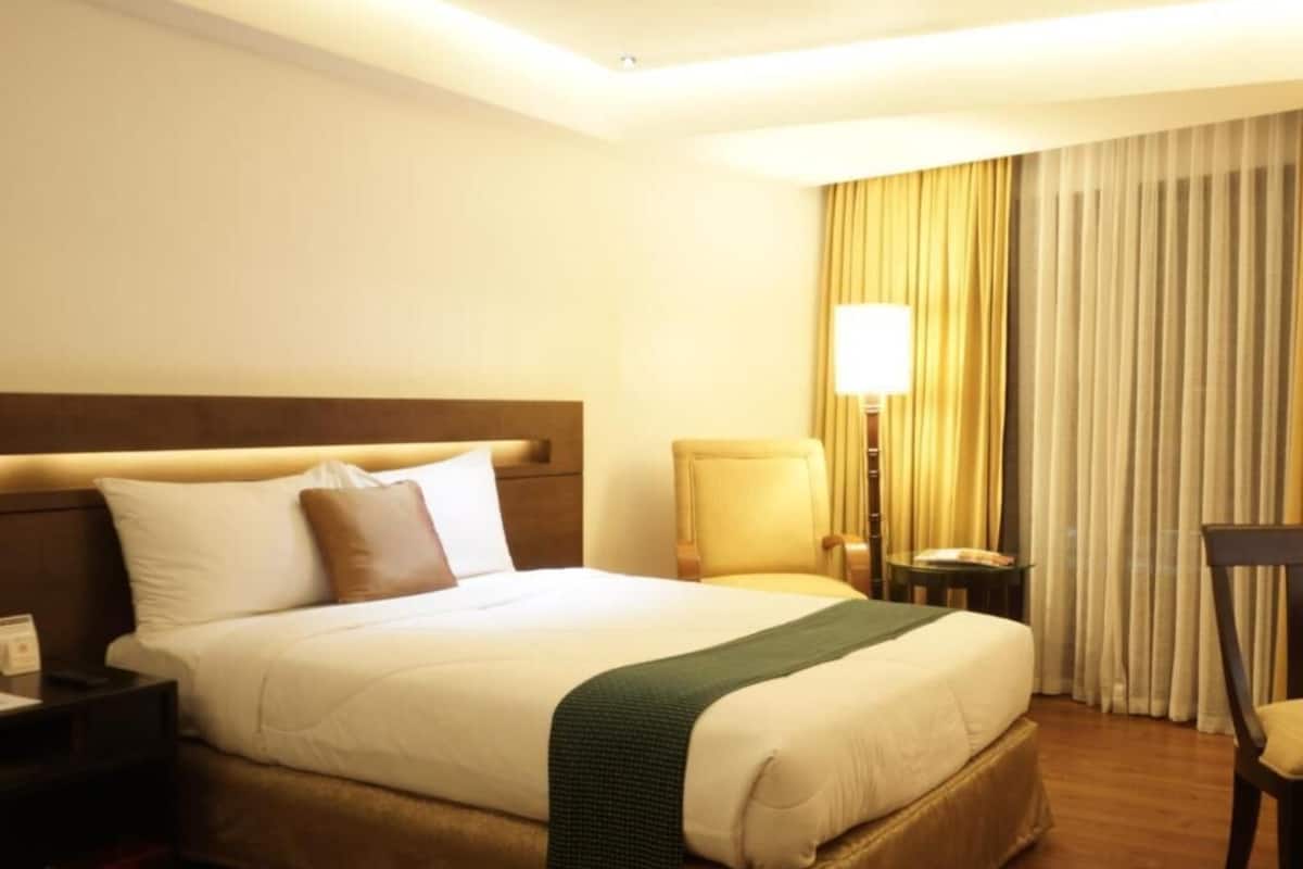 A hotel room with a large bed, a bedside table, a chair, a lamp, and a window with curtains.