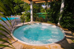 A hot tub surrounded by lush greenery and a pool.