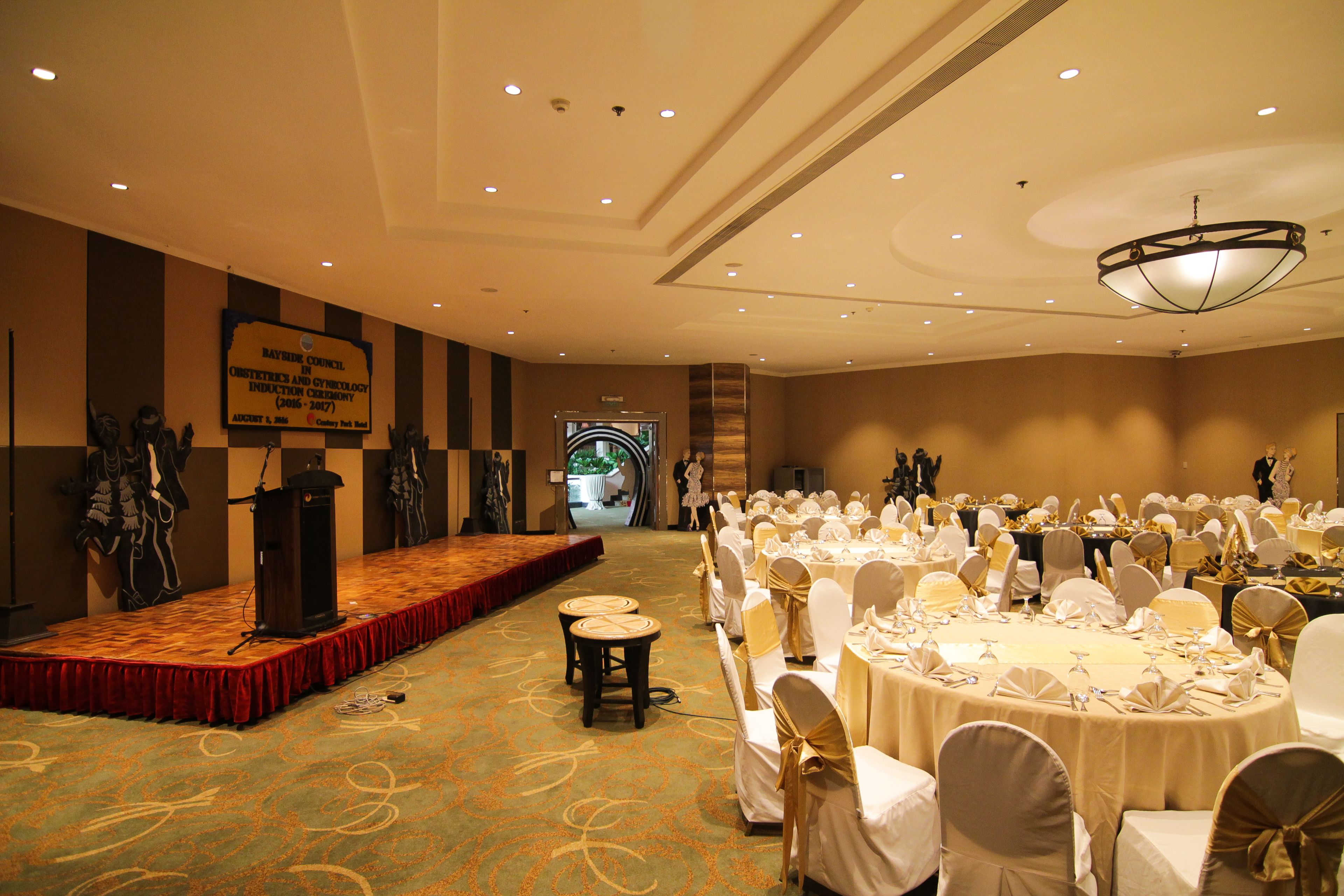 A banquet hall with round tables set for a formal event, a stage with a podium, and a banner on the wall.