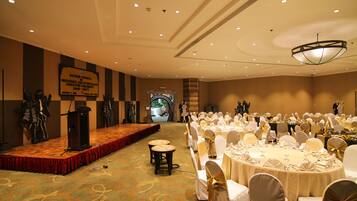 A banquet hall with round tables set for a formal event, a stage with a podium, and a banner on the wall.