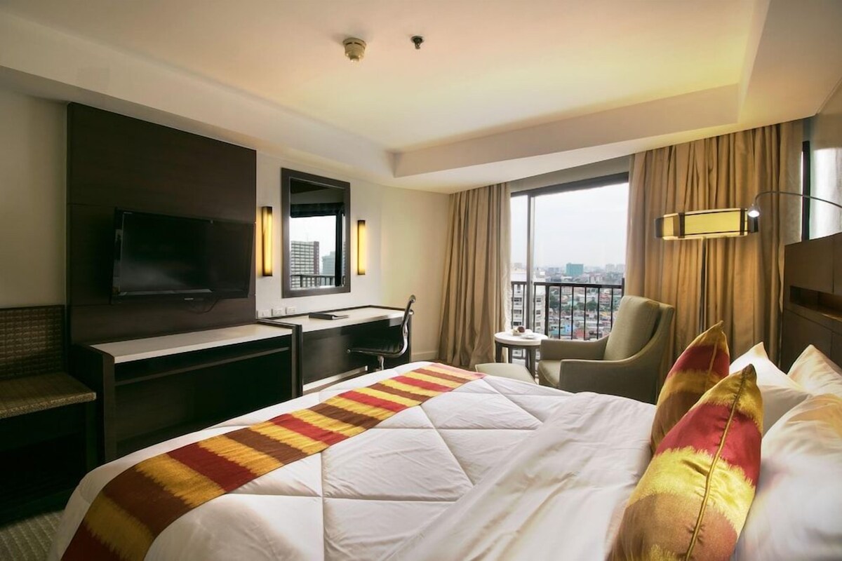 A hotel room with a bed, a desk, a chair, a TV, and a view of the city.