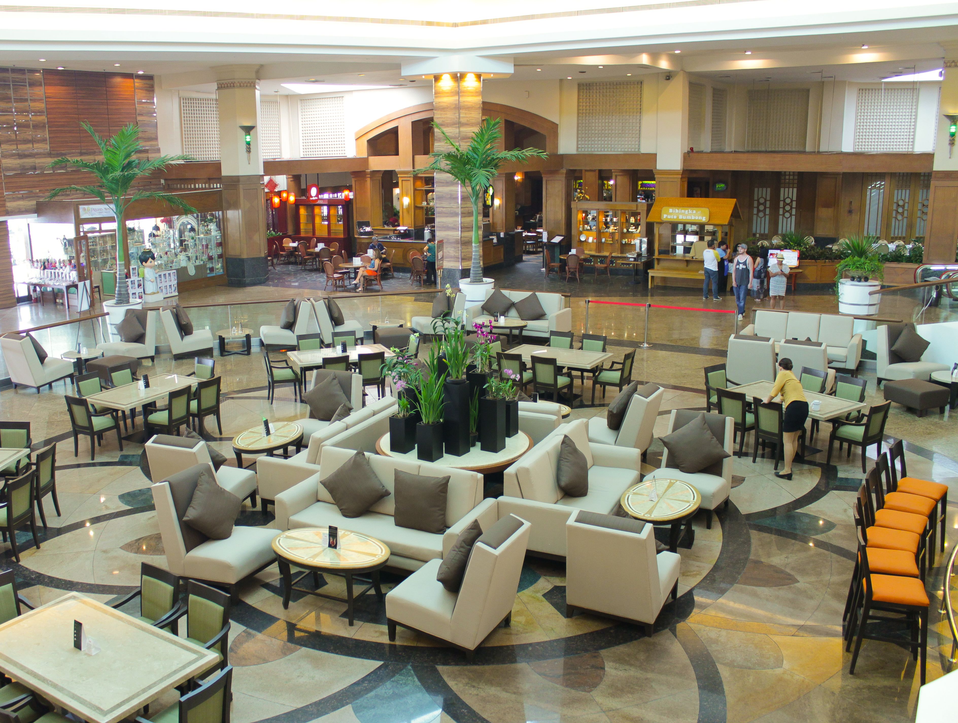 A spacious lobby with multiple seating areas, including sofas and tables, and a central plant arrangement.