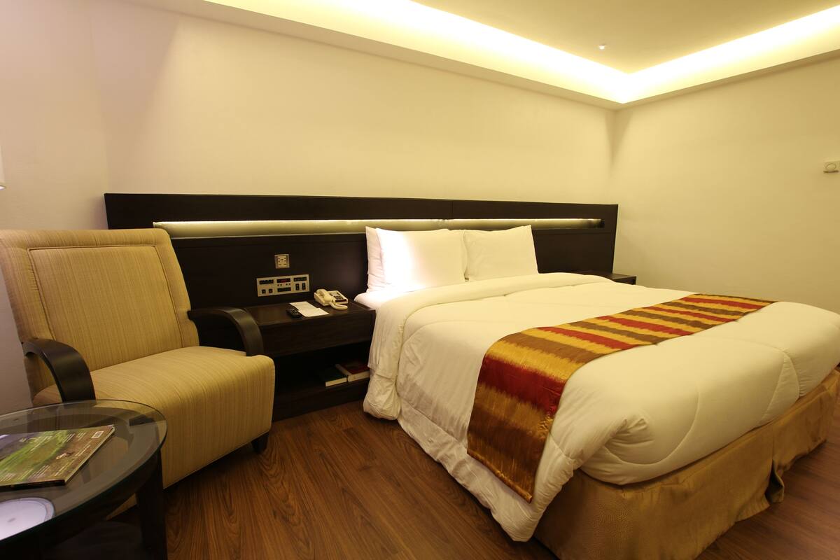 A hotel room with a bed, a chair, a bedside table, and a small table with a magazine.