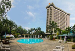 A hotel with a swimming pool, lounge chairs, and palm trees.