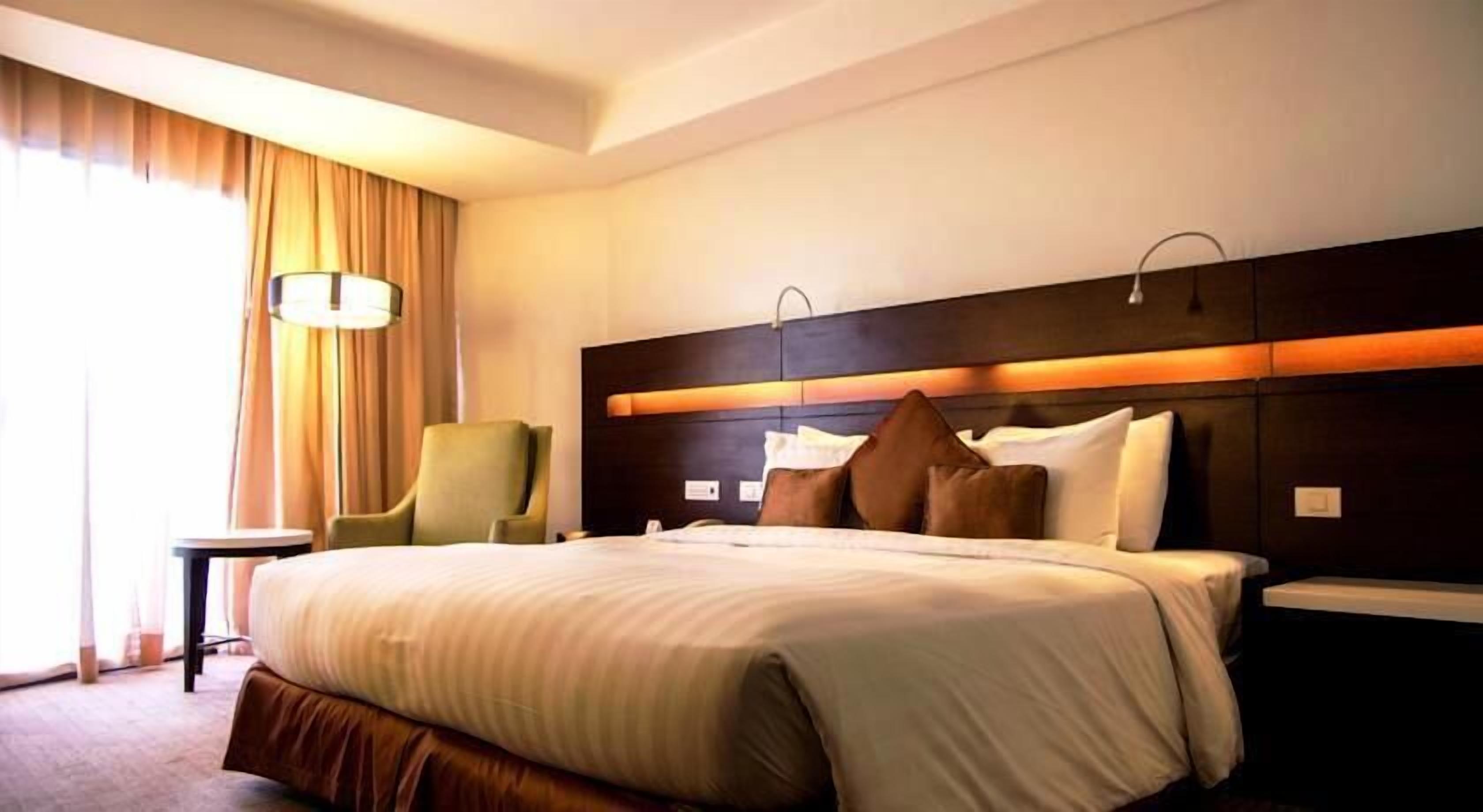 Une chambre d’hôtel avec un grand lit, une chaise, une table de chevet et une lampe.