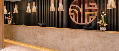 A reception area with a modern design, featuring a reception desk, multiple pendant lights, and decorative wall panels.