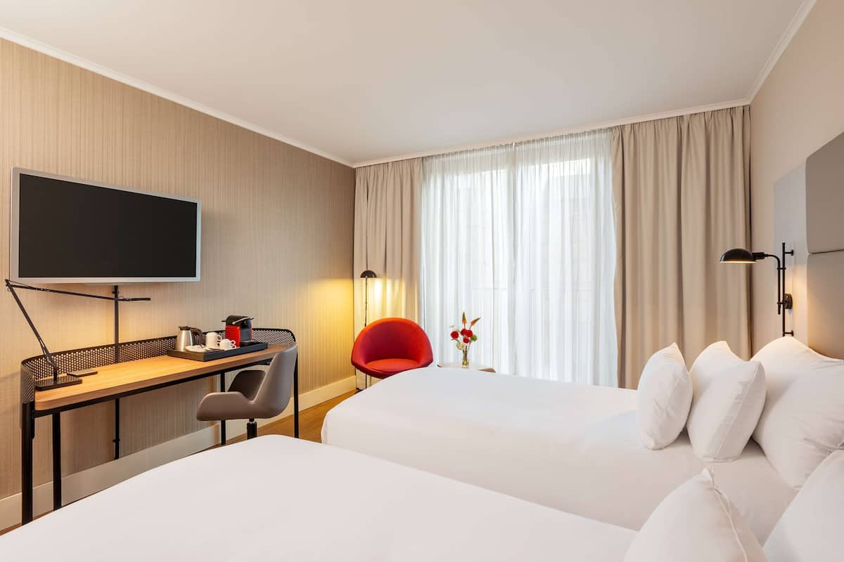 A hotel room with a bed, a desk with a chair, a TV, and a window with curtains.