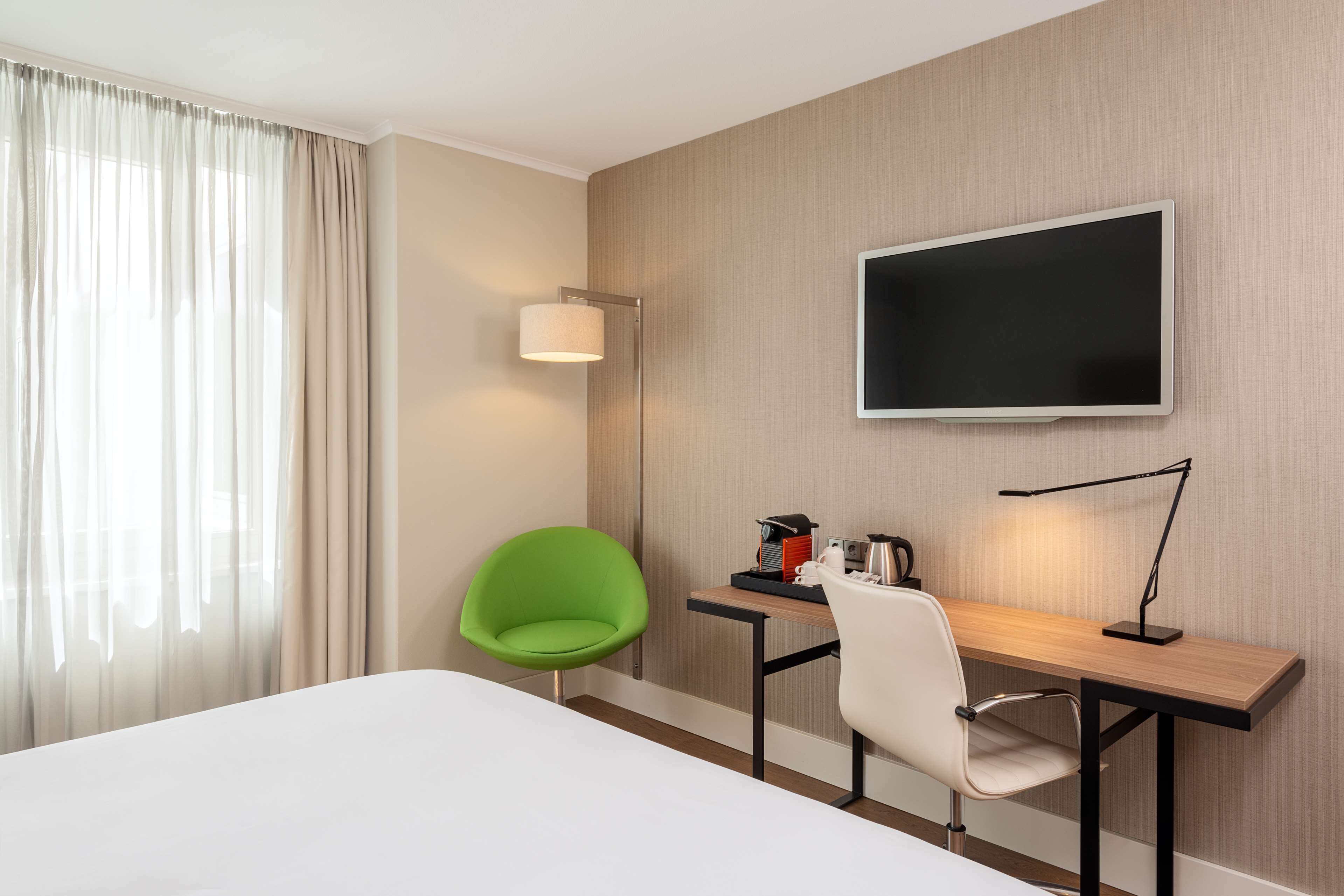 A hotel room with a bed, a desk with a chair, a television, and a lamp.