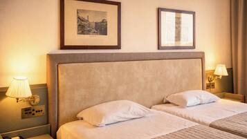 A hotel room with two beds, a nightstand with a phone, and two wall-mounted lamps.
