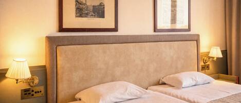 A hotel room with two beds, a nightstand with a phone, and two wall-mounted lamps.