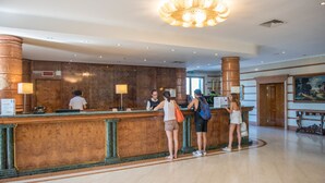 A hotel reception area with a marble counter, a chandelier, and a painting on the wall.